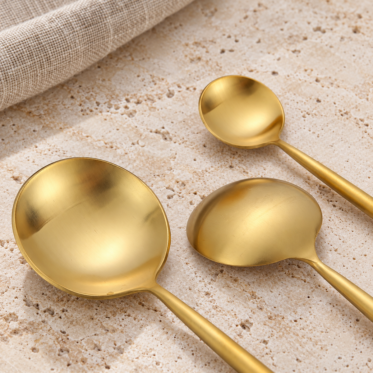 Halden gold stainless steel spoon heads on warm travertine