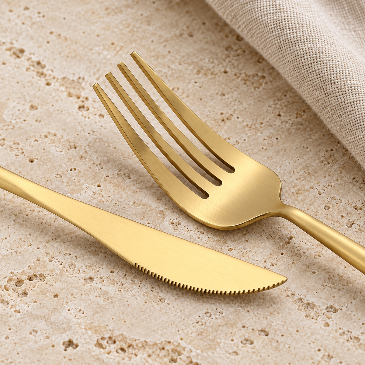 Halden gold stainless steel fork and table knife detail on warm travertine