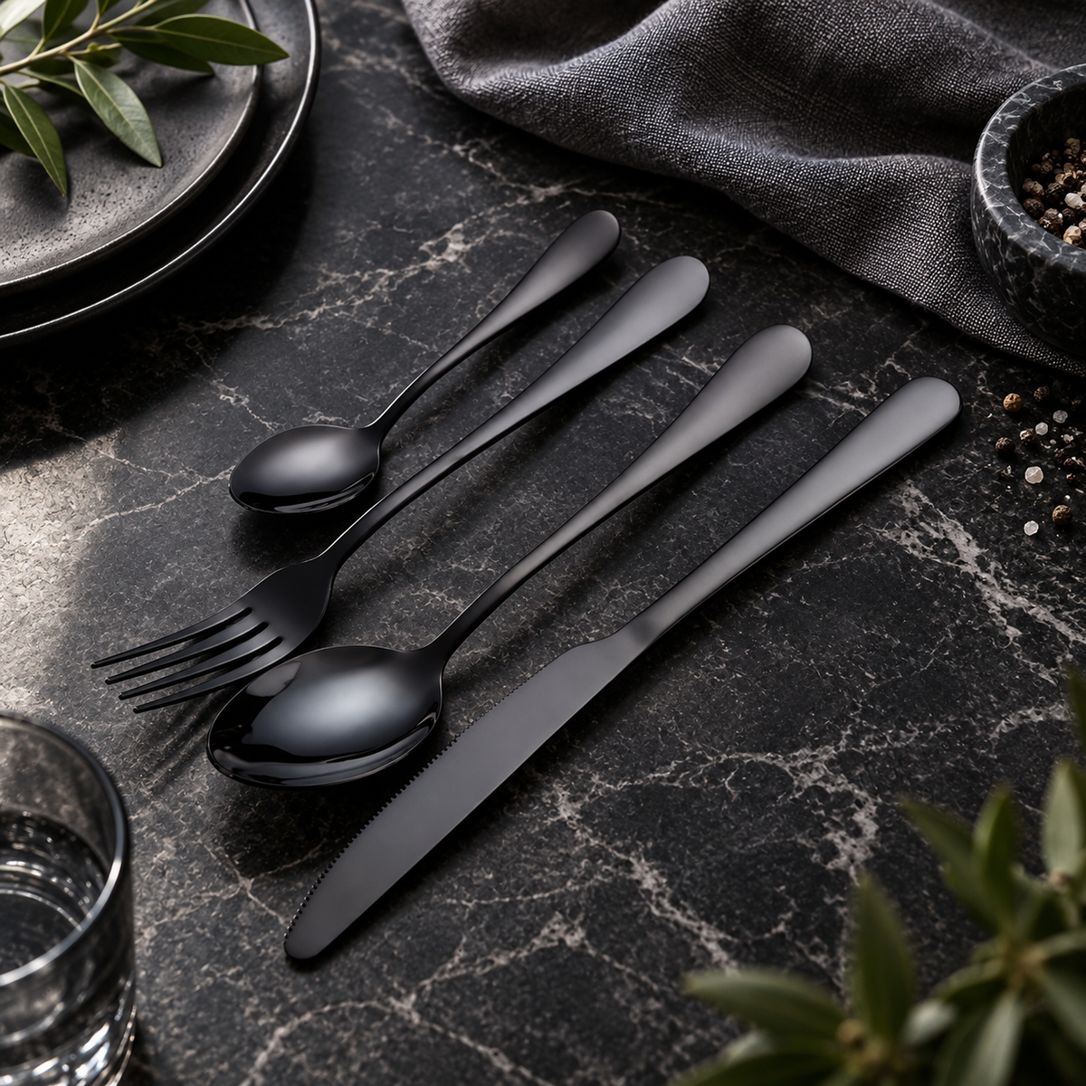 Tove black stainless steel flatware set on a dark stone dining table