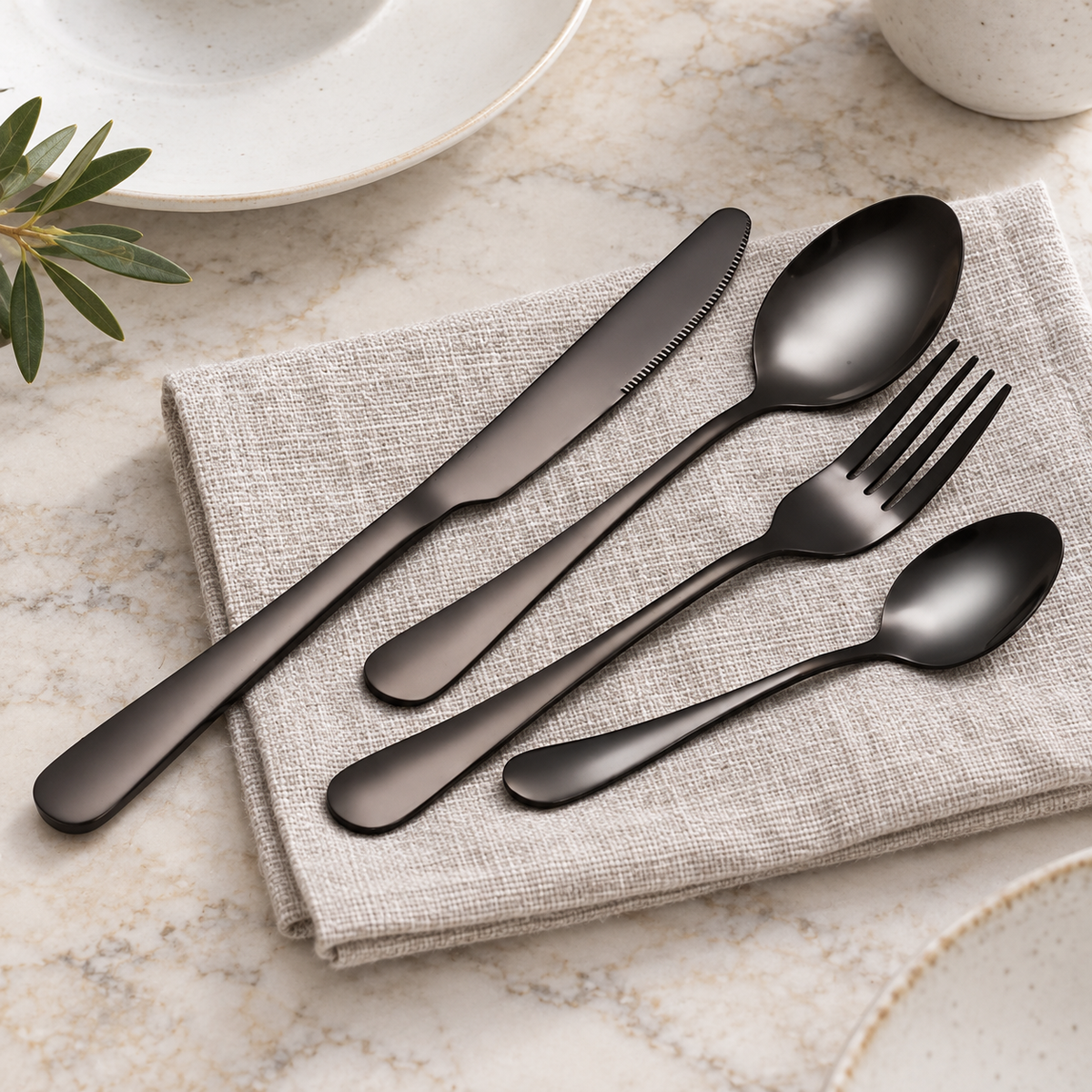 Brenna matte black stainless steel flatware on neutral linen and a pale stone dining table