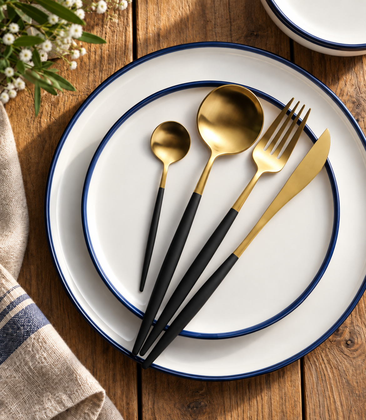 Astrid gold and black four-piece flatware set on blue-rimmed white plates