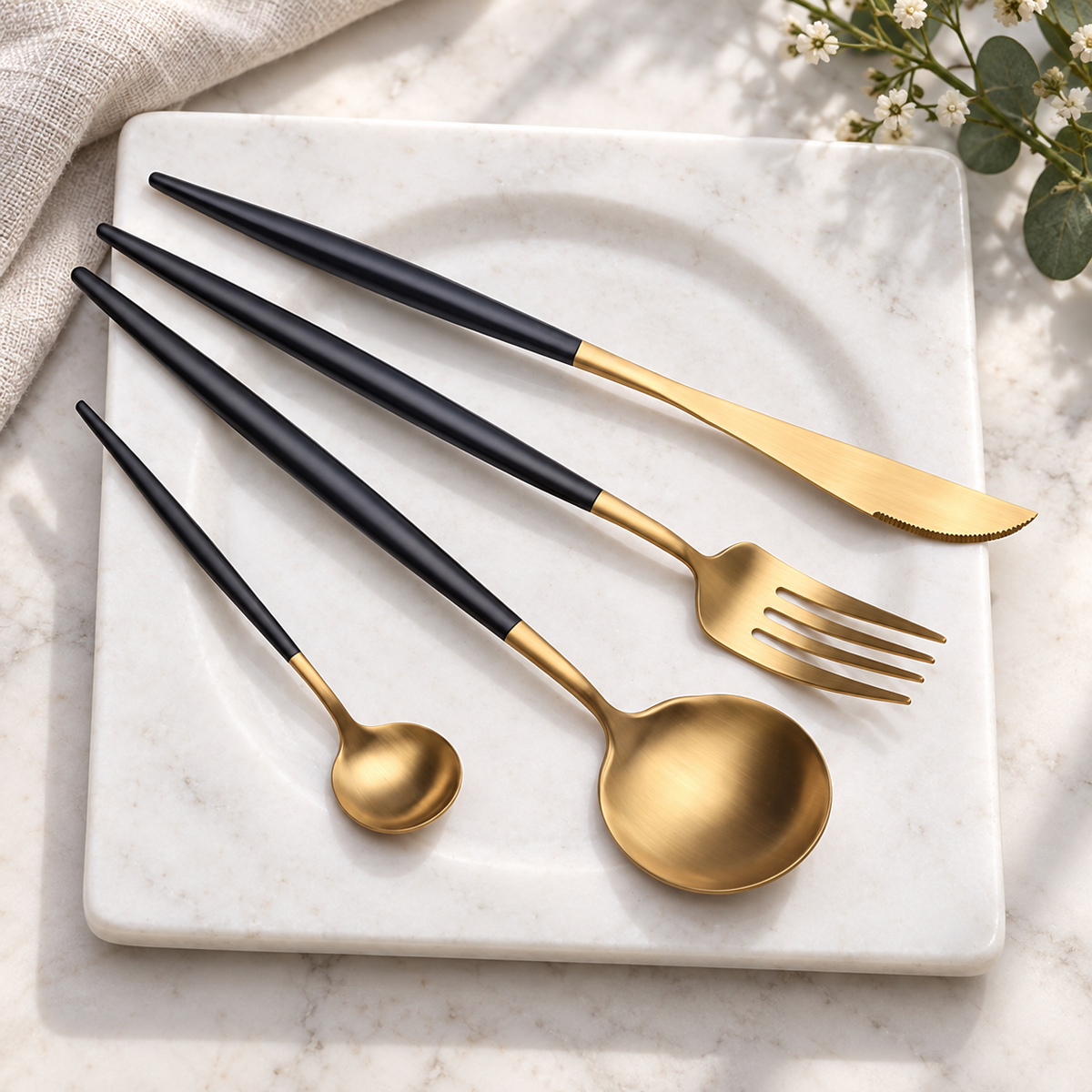 Astrid gold and black four-piece flatware set on a warm white stone tray