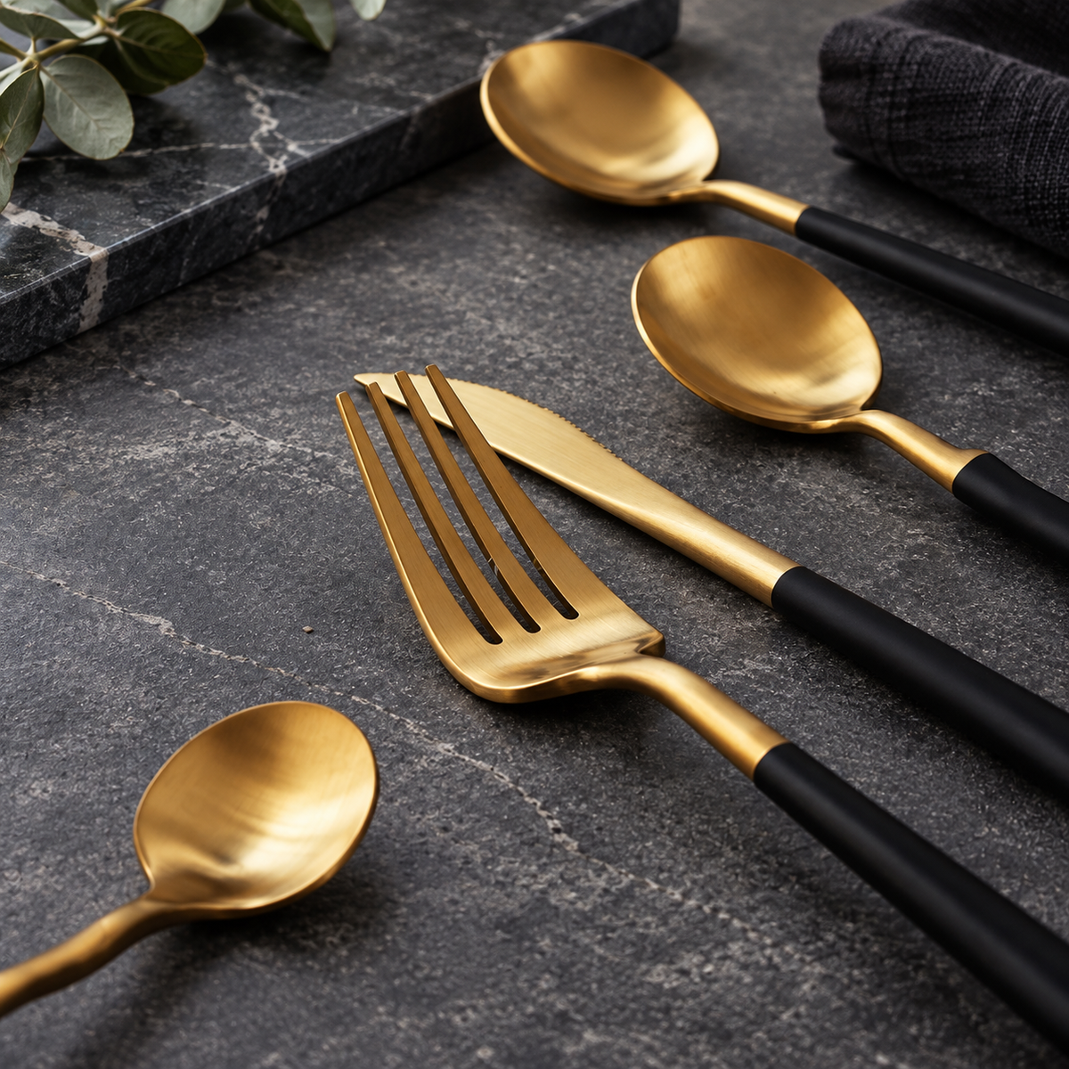 Astrid gold and black flatware close-up on a dark charcoal stone surface