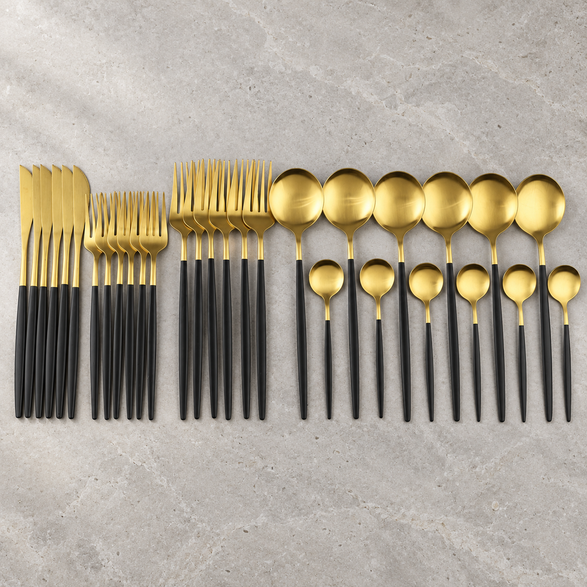 Lykke black and gold stainless flatware set arranged on pale stone