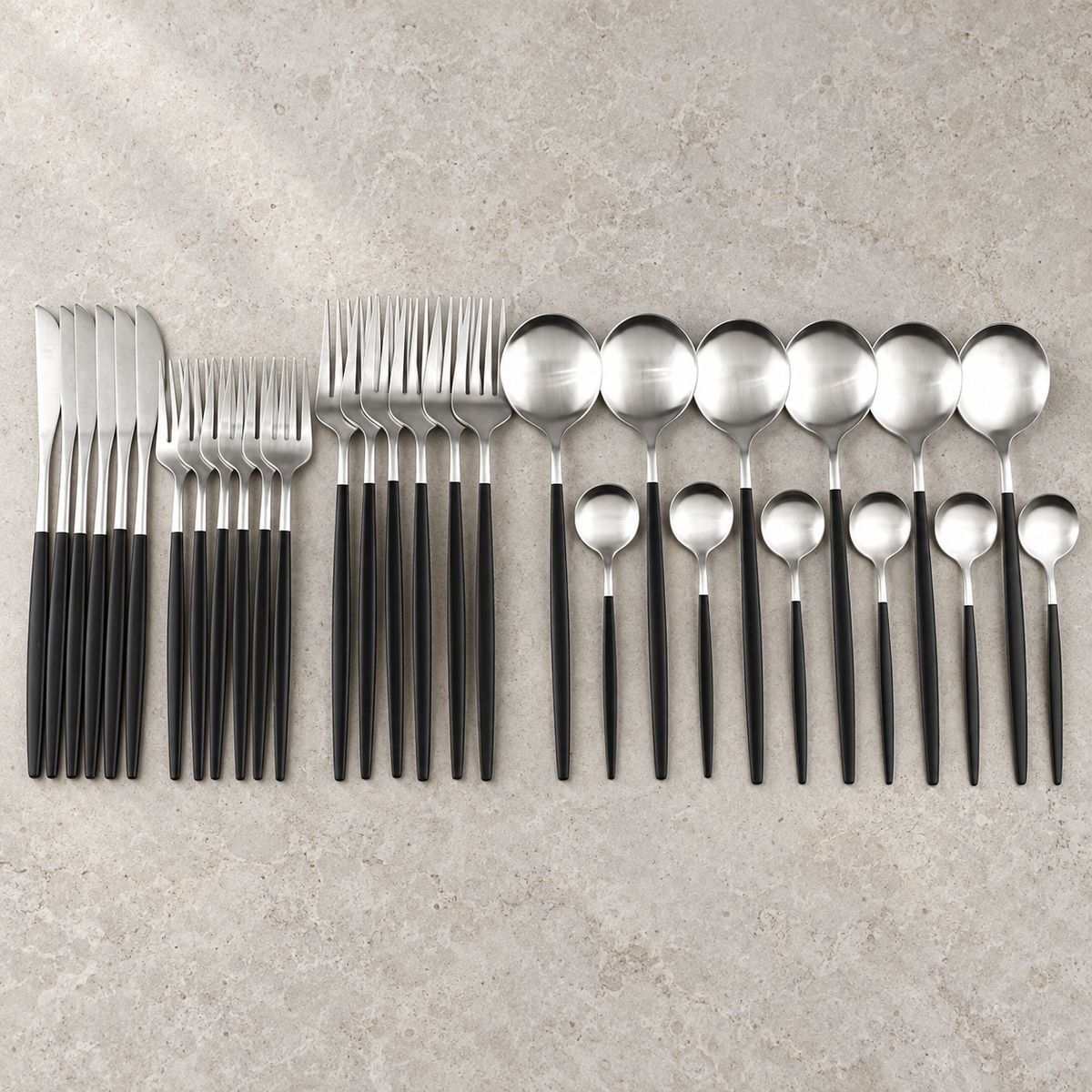 Lykke black and silver stainless flatware set arranged on pale limestone