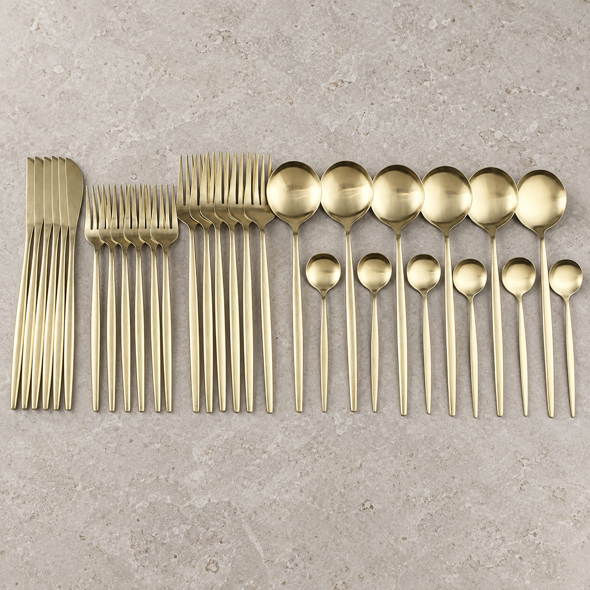 Lykke champagne gold stainless flatware set arranged on light limestone