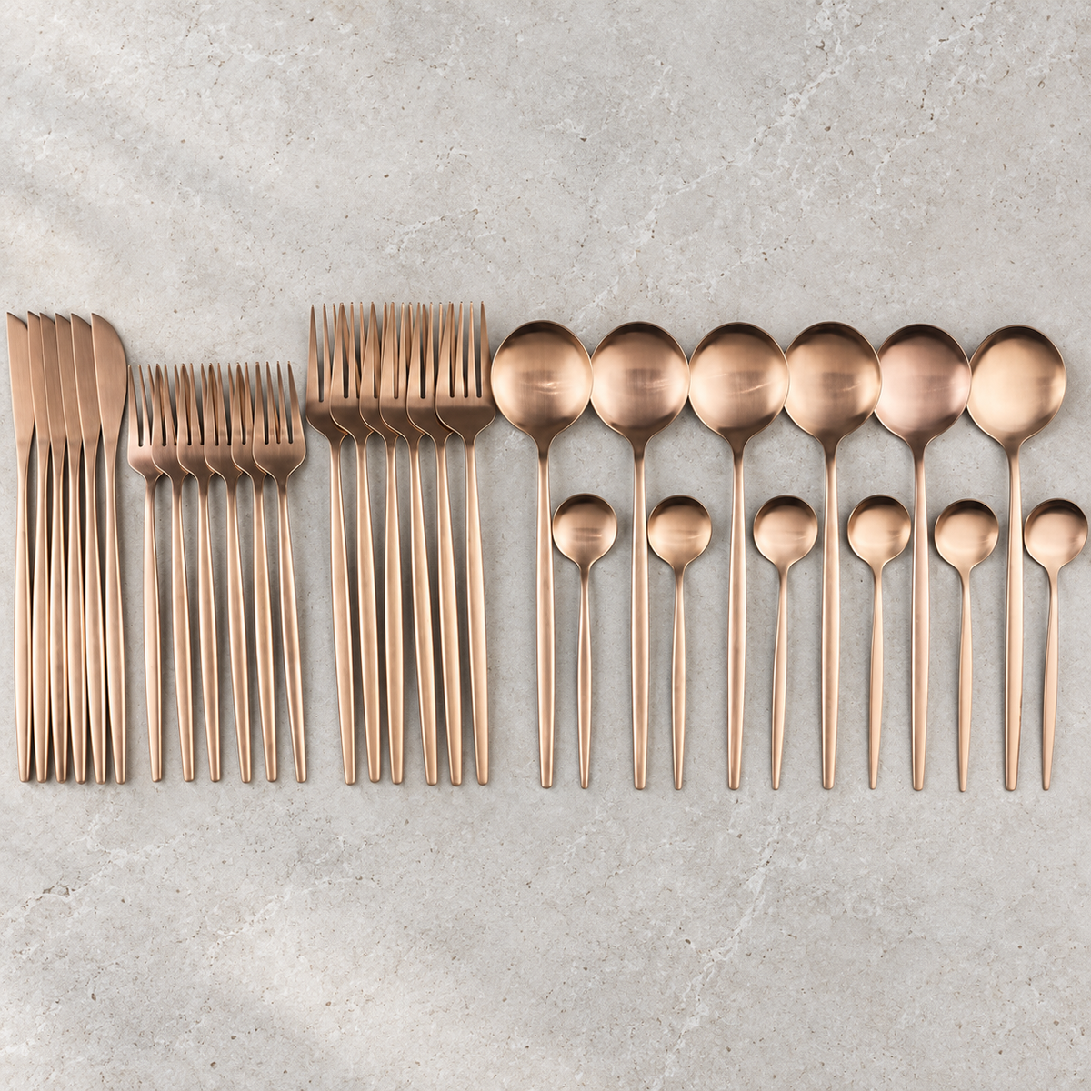 Lykke rose gold stainless flatware set arranged on pale limestone