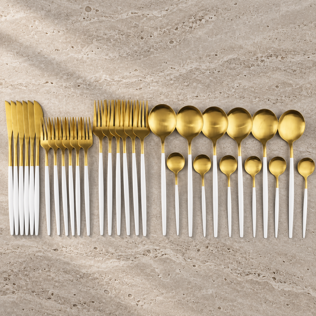 Lykke white and gold stainless flatware set arranged on warm stone