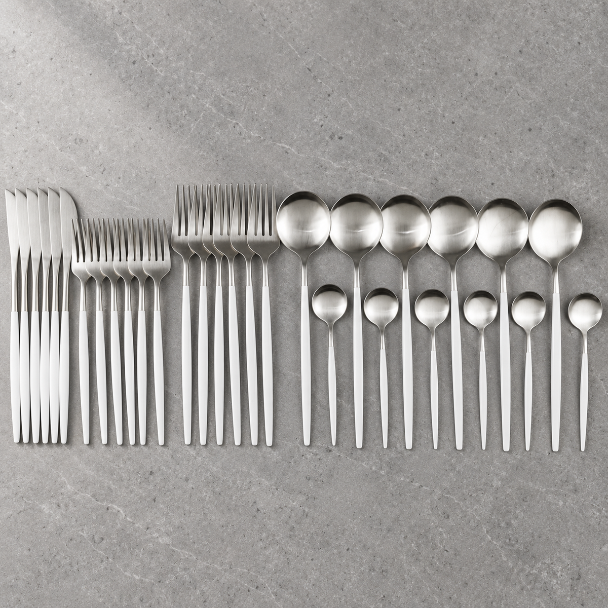 Lykke white and silver stainless flatware set arranged on grey stone