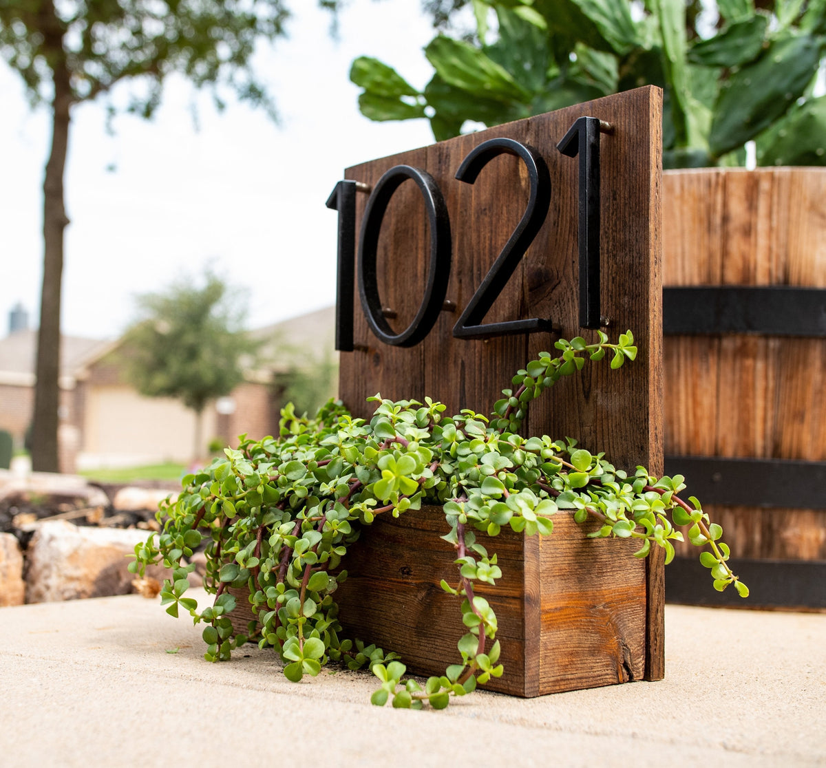 Black zinc alloy house numbers 0, 2 and 1 mounted on wood beside a planter
