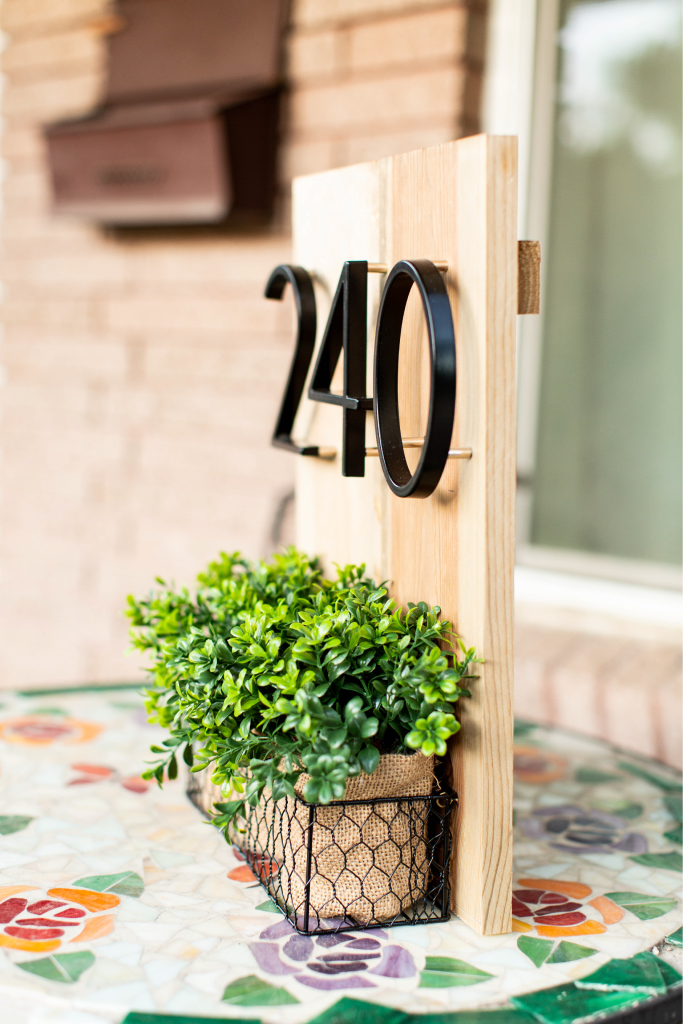 Black zinc alloy house numbers 2, 4 and 0 on a wood address plaque with planter