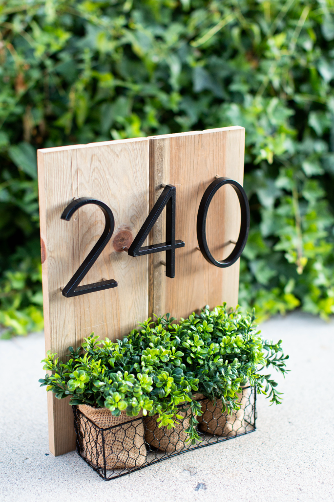 Black zinc alloy house numbers 2, 4 and 0 on wood above three small planters