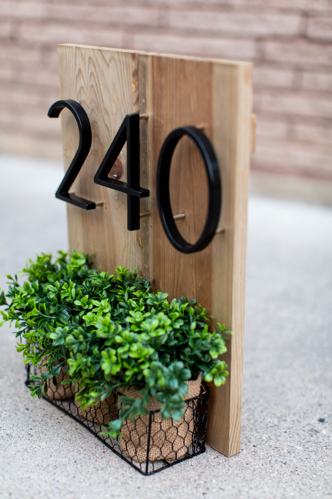 Angled view of black zinc alloy house numbers 2, 4 and 0 on a wood plaque