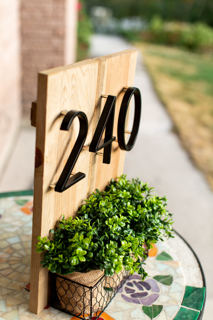 Black zinc alloy house numbers 2, 4 and 0 on wood beside a small planter