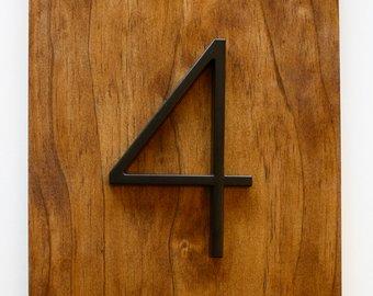 Black zinc alloy house number 4 mounted on a wood surface