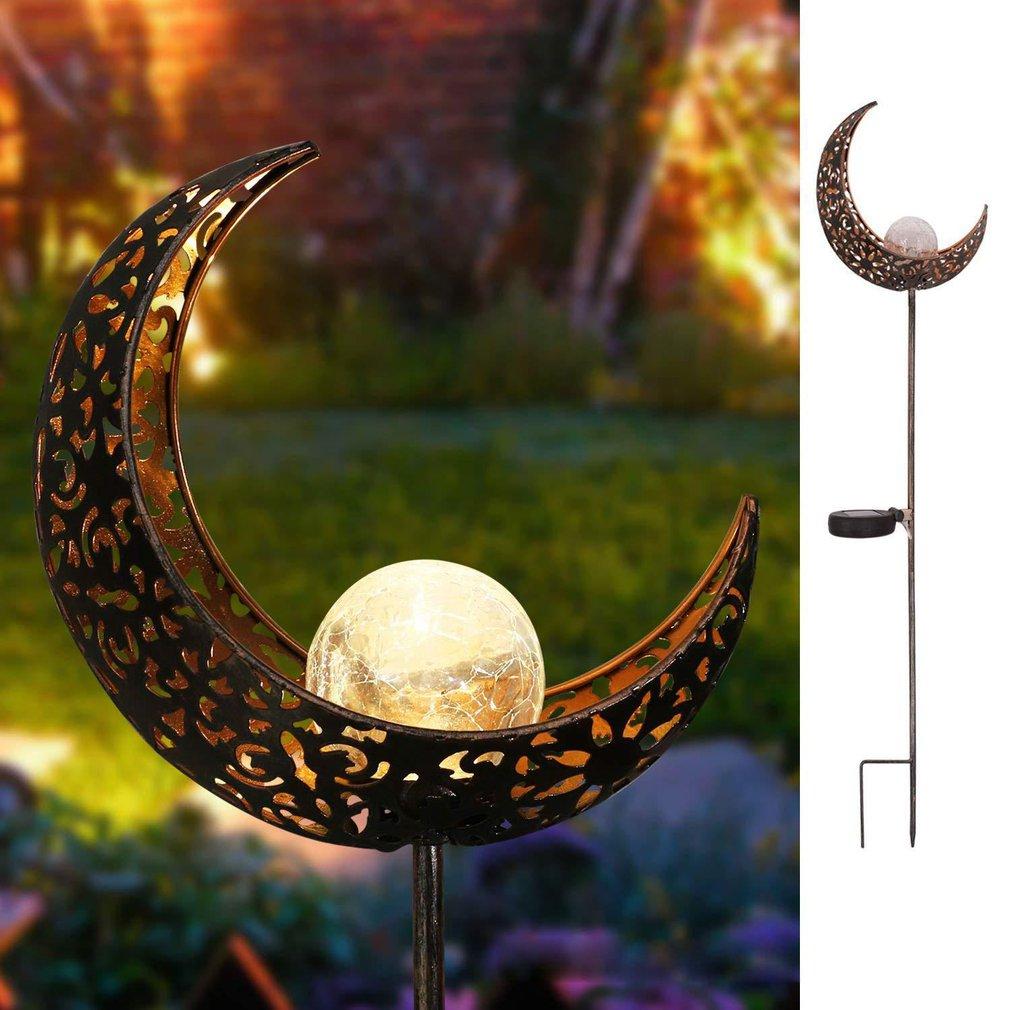 Solar crescent moon garden stake glowing in a garden beside a full-length product view