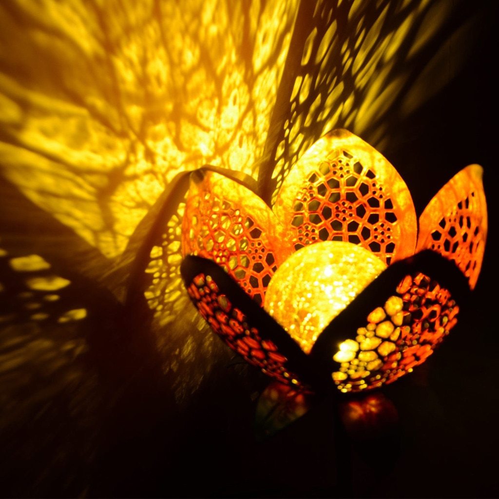 Idun gold flower stake light glowing in close-up with pierced-petal shadows