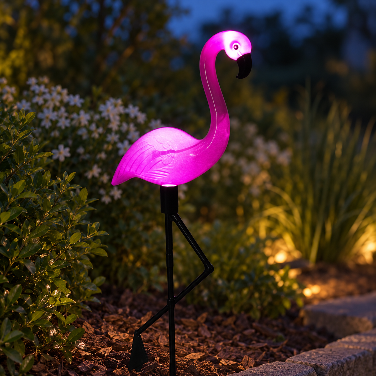 Single solar flamingo garden stake light glowing in a blue-hour garden close-up
