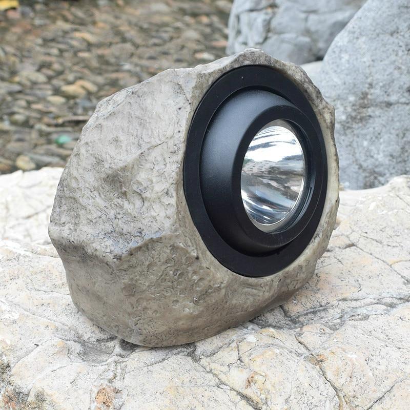 Stone-effect solar garden light angled on pale rocks beside a garden pond