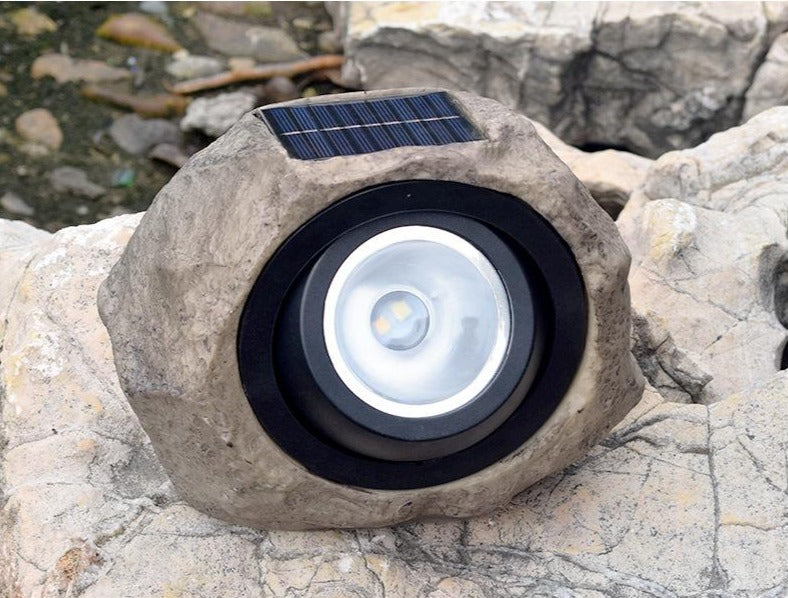 Stone-effect solar garden light front view resting among pale garden rocks