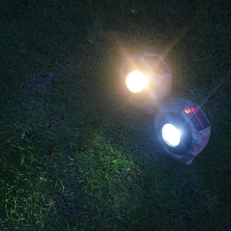 Two stone-effect solar garden lights casting warm and cool light across a lawn