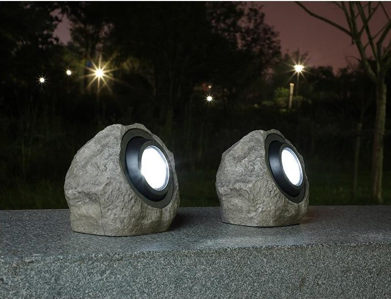 Two stone-effect solar garden lights glowing on a garden ledge at night