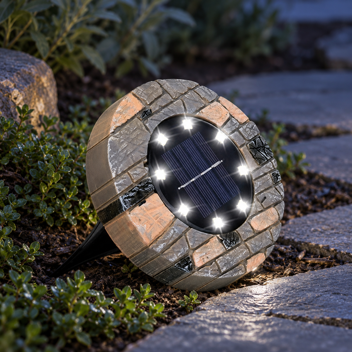 Stone solar pathway light with white LEDs glowing beside pavers and groundcover at twilight